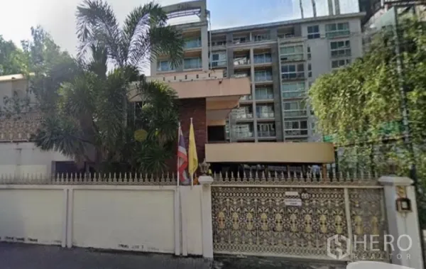 Detached House for sale in Khlong Toei, Bangkok - Gated detached house in Khlong Toei with ornate fence, mature palm trees, and a mid-rise building in the background.