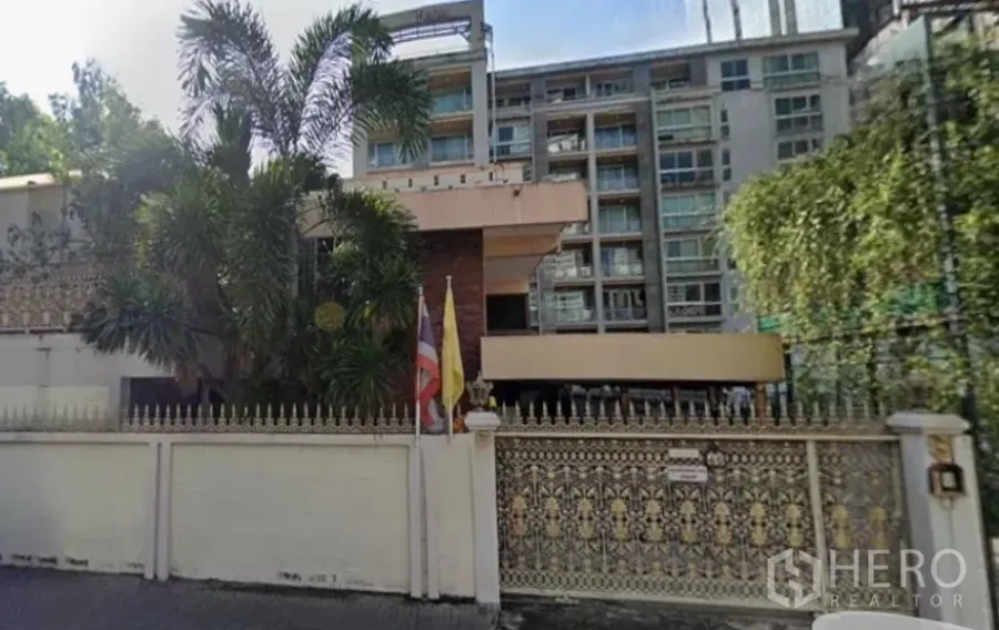 Detached House for sale in Khlong Toei, Bangkok - Gated detached house in Khlong Toei with ornate fence, mature palm trees, and a mid-rise building in the background.
