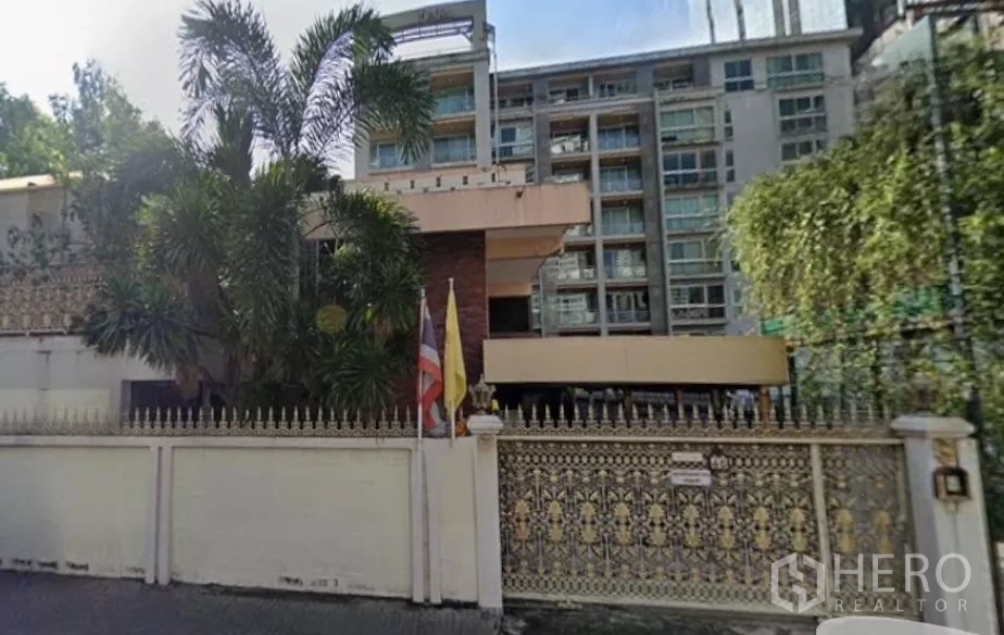 Detached House for sale in Khlong Toei, Bangkok - Gated detached house in Khlong Toei with ornate fence, mature palm trees, and a mid-rise building in the background.
