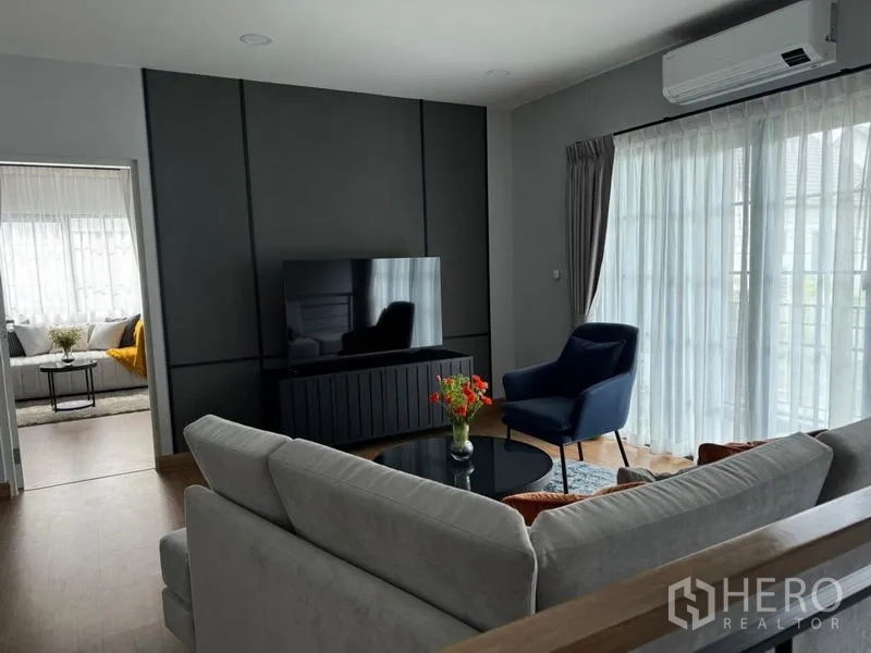 Detached House for rent or sale in Bang Phli, Samut Prakan - Upstairs family lounge with sectional sofa, TV wall unit, blue armchair and sheer curtains.