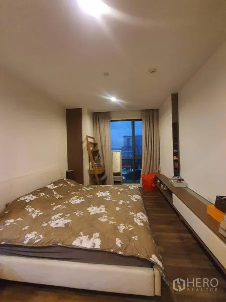 Condominium for sale in Bangkok - Bedroom with double bed, wood floors, and a floor-to-ceiling window leading to a city-view balcony.