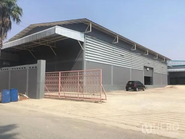 工厂 出售在Bang Lamung, Chon Buri - 灰色厂房外观，带大门与宽阔混凝土场地，便于卡车进出。