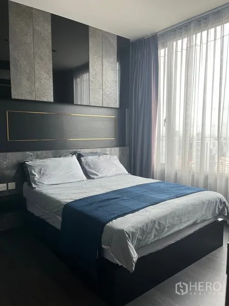 公寓 出租在Watthana, Bangkok - 卧室温馨，大窗俯瞰城市，深色背景墙与镜面装饰。