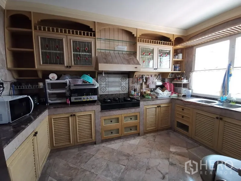 独立式住宅 出售在Phra Khanong, Bangkok - U形厨房，木质橱柜、彩绘玻璃柜门、燃气灶与大理石台面。