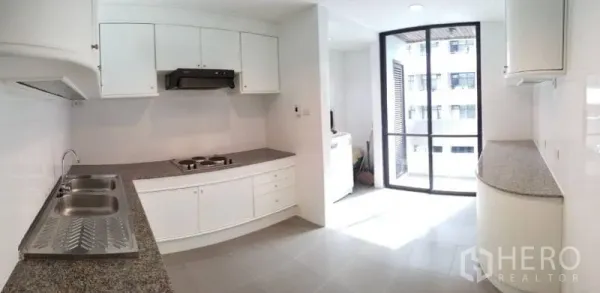 Condominium for rent in Sathon, Bangkok - White U-shaped kitchen with granite countertops and sliding glass door to balcony.