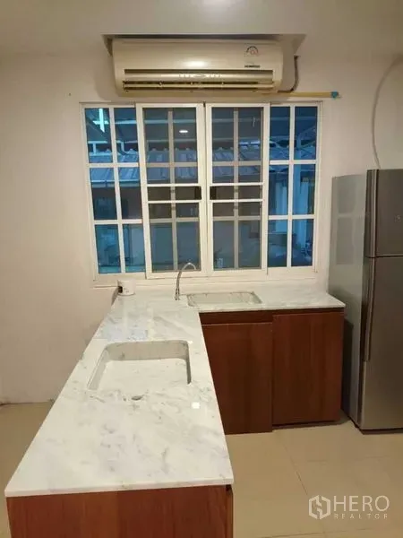 Townhouse for rent in Bang Kapi, Bangkok - Light kitchen with L-shaped marble countertops, sink, window, and stainless-steel refrigerator.
