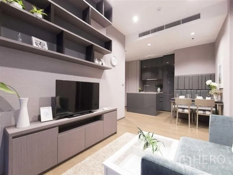 Condominium for rent in Bang Rak, Bangkok - Living area with TV console and floating shelves, opening toward the kitchen and dining zone.