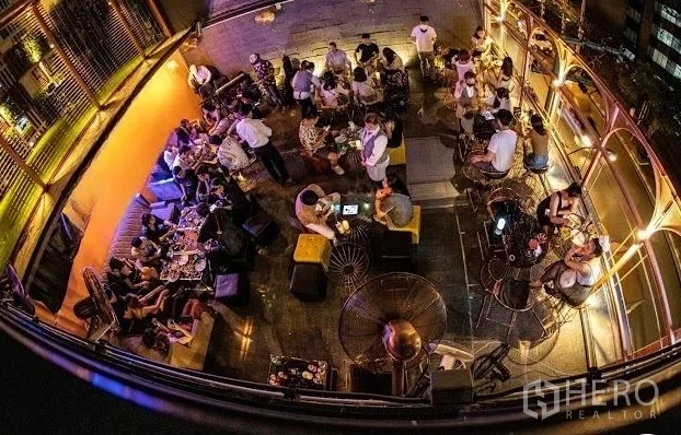 พื้นที่ขายปลีก ให้เช่า - ภาพมุมสูงของรูฟท็อปเลานจ์ โต๊ะนั่ง แสงไฟโทนอุ่น และวิวเมือง เหมาะสำหรับสังสรรค์