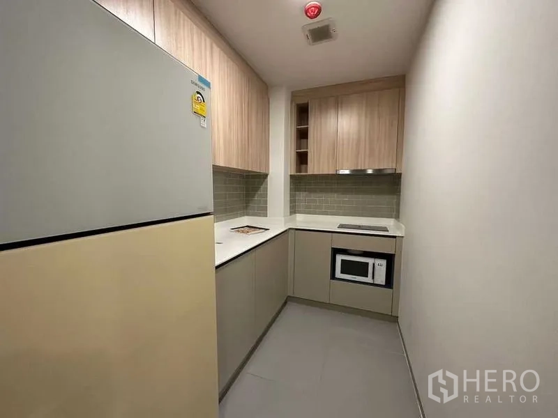 公寓 出租在Ratchathewi, Bangkok - 走廊式厨房，嵌入式灶台、微波炉、浅木柜与地铁砖背景墙。