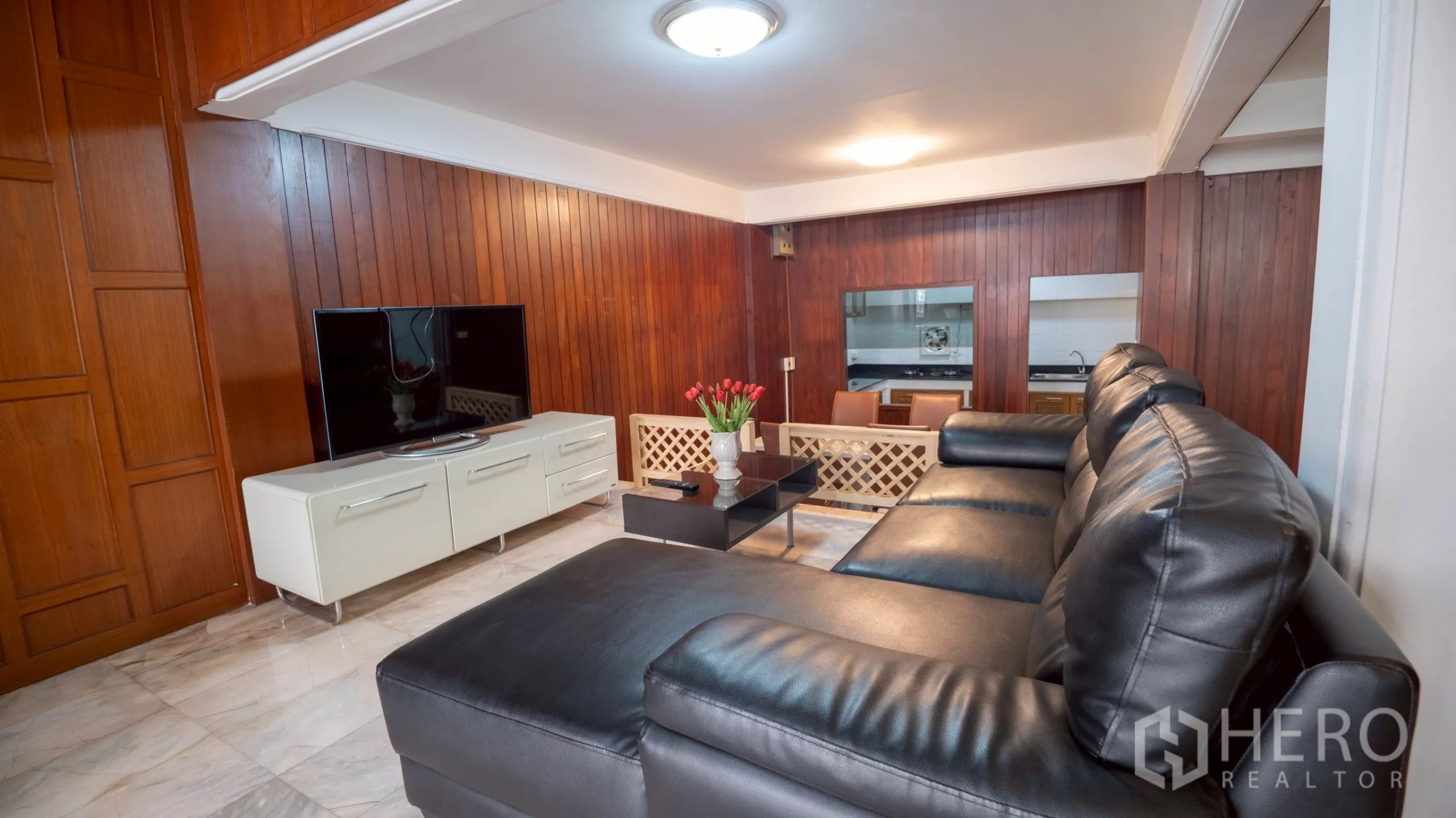 Townhouse for rent in Khlong Toei, Bangkok - Living room with leather sectional sofa, TV console and wood-paneled walls.