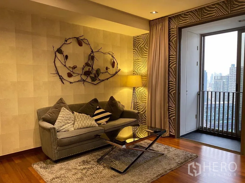 公寓 出租在Khlong Toei, Bangkok - 温馨客厅，灰色沙发、落地灯与木地板，连接阳台可赏城市景观。