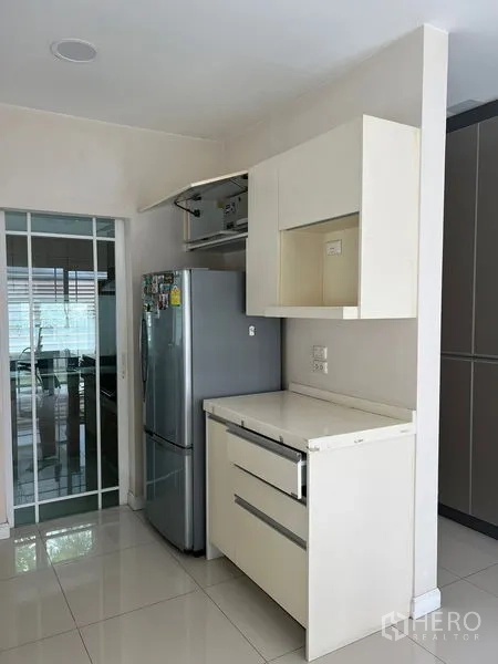 Detached House for rent in Bang Kapi, Bangkok - Pantry space with tall refrigerator and white cabinetry beside a sliding kitchen door.