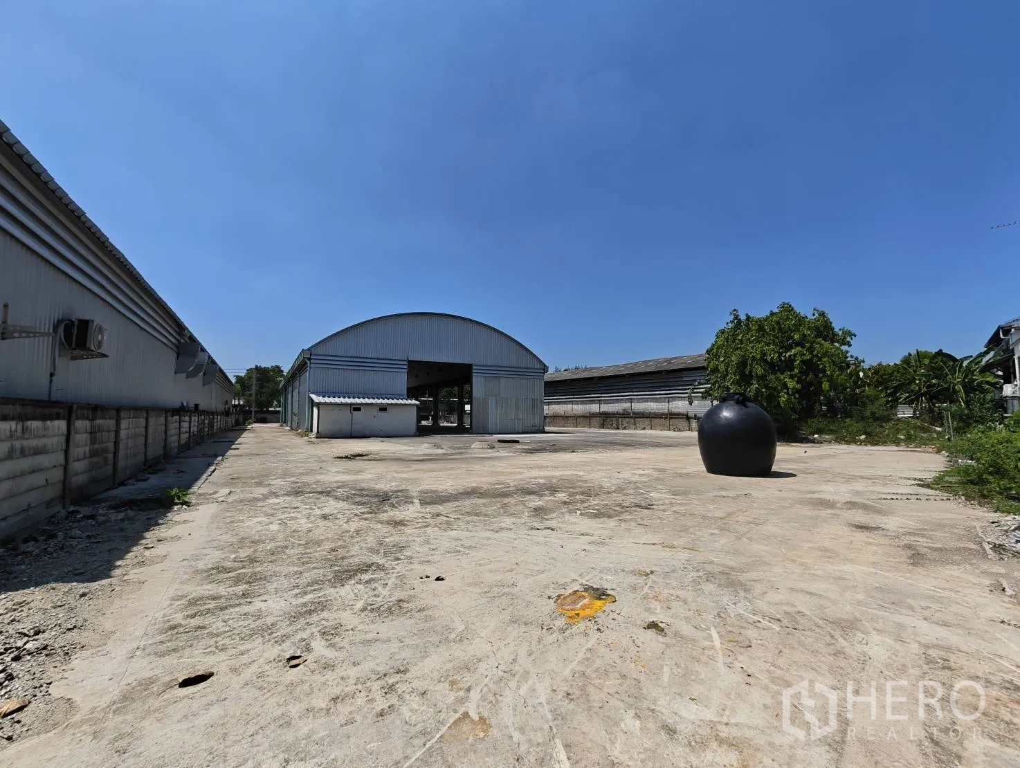 仓库 for rent in Lak Si, Bangkok - 宽阔的混凝土场地通向拱形金属仓库，周边有围墙。