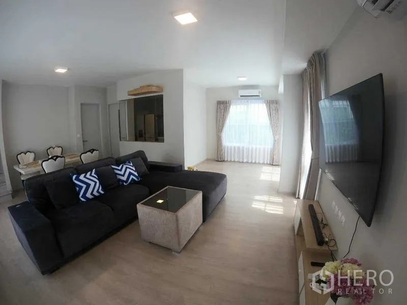 Townhouse for rent - Open-plan living and dining space with sectional sofa, TV wall, and kitchen window.