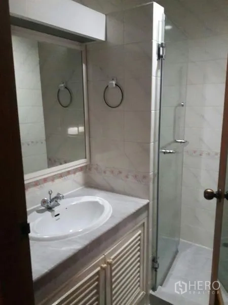 Condominium for rent in Pathum Wan, Bangkok - Bathroom with vanity, mirror, and glass‑enclosed shower in neutral tiles.