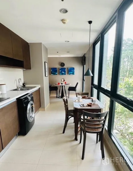 Condominium for rent in Watthana, Bangkok - Open‑plan kitchen with long counter and two dining areas by large windows.
