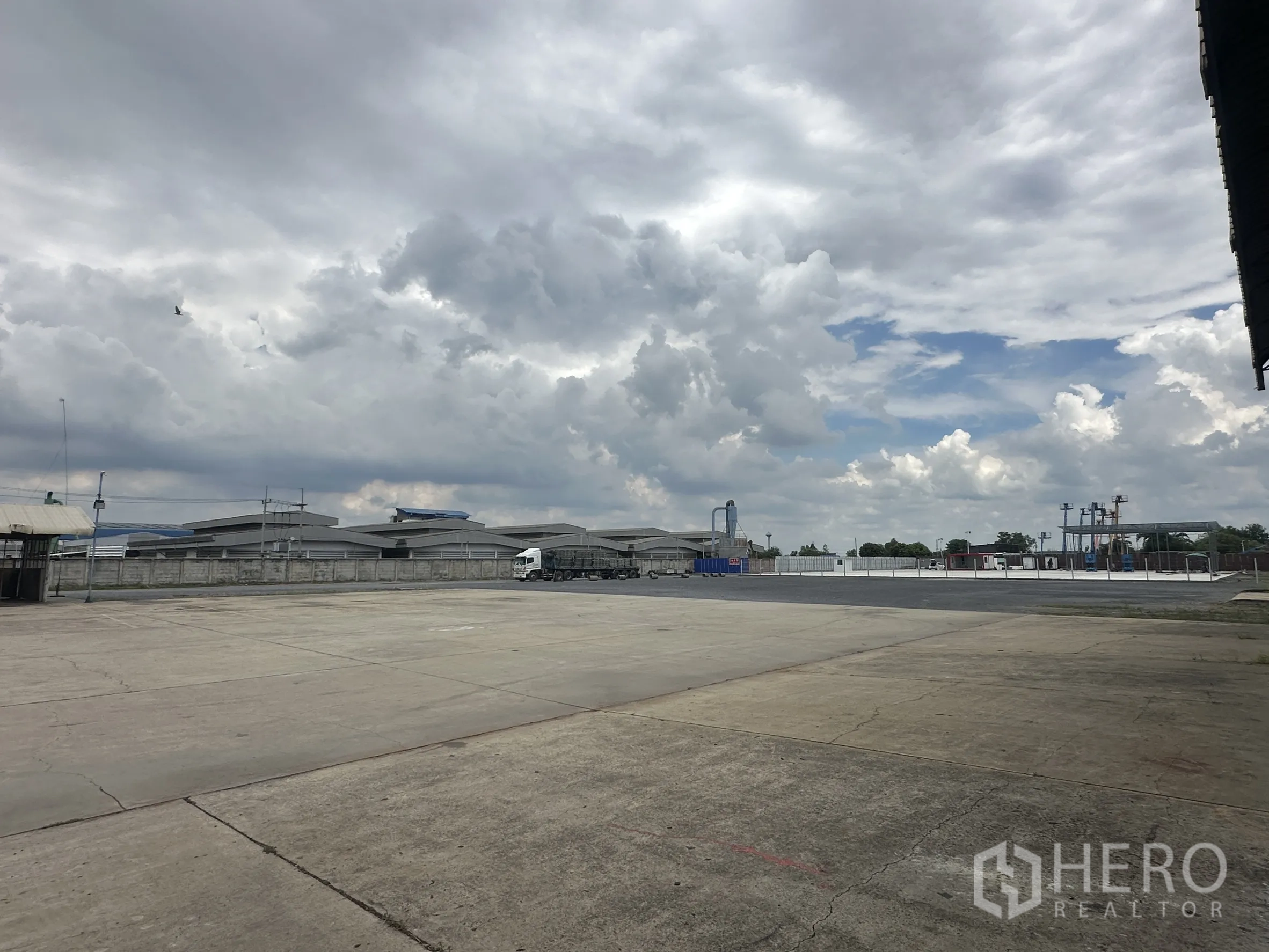 Land for rent in Wang Noi, Phra Nakhon Si Ayutthaya - Wide concrete yard with perimeter wall and industrial buildings in the distance.