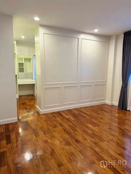 Detached House for rent in Samut Prakan - Bedroom with paneled accent wall, wood floors, and a dressing area with vanity.