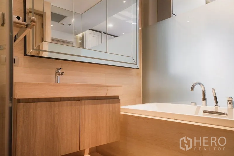 Condominium for rent or sale in Watthana, Bangkok - Bathroom with large framed mirror, wood vanity and bathtub behind frosted glass partition.
