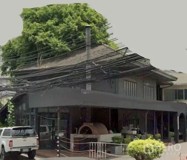 零售空间 出租在Watthana, Bangkok - 曼谷瓦塔那区两层转角商铺，整面玻璃立面，带遮棚前廊与户外砖炉设施。