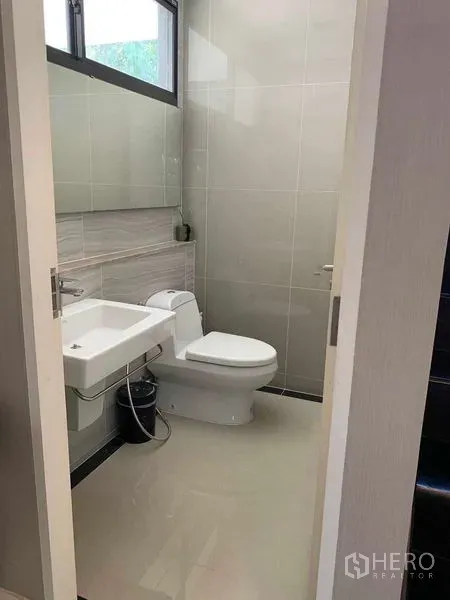 Detached House for rent or sale in Bang Phli, Samut Prakan - Compact bathroom with white sink, toilet, light gray tiles and a window.