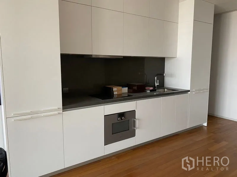 คอนโด ให้เช่า - ภาพระยะใกล้ของครัวสีขาวสมัยใหม่ เคาน์เตอร์ ซิงก์ และเตาอบบิลท์อิน