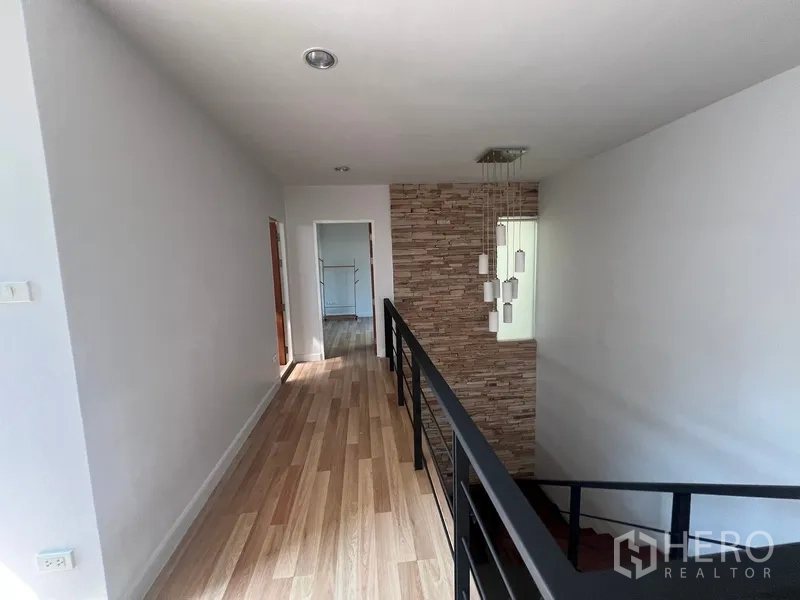 Townhouse for rent in Din Daeng, Bangkok - Upper landing with wood floors, metal railing and stone feature wall leading to bedrooms.
