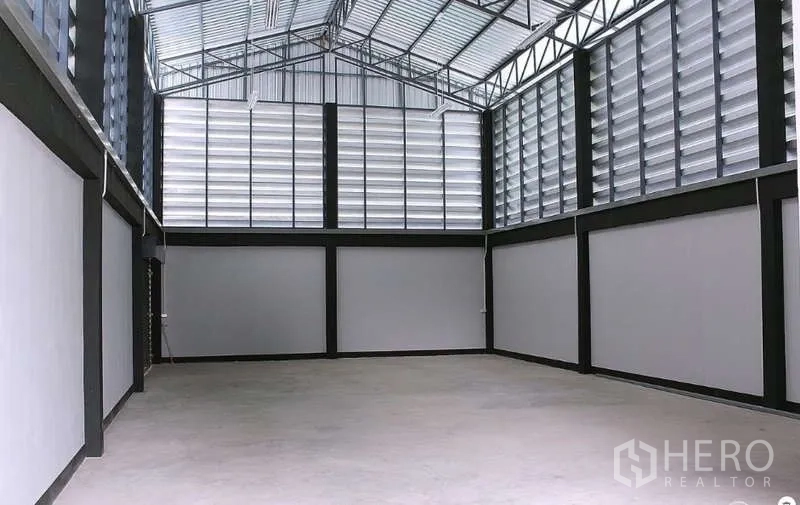 Warehouse for sale in Pathum Thani - Spacious warehouse interior with high steel trusses, louvered walls and polished concrete floor.