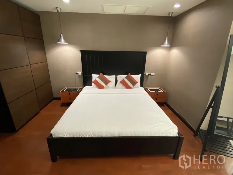 คอนโด ให้เช่าในWatthana, Bangkok - ห้องนอนใหญ่ เตียงไม้สีเข้ม ชุดเครื่องนอนสีขาว โคมแขวนข้างเตียง ผนังโทนสีน้ำตาล พื้นไม้