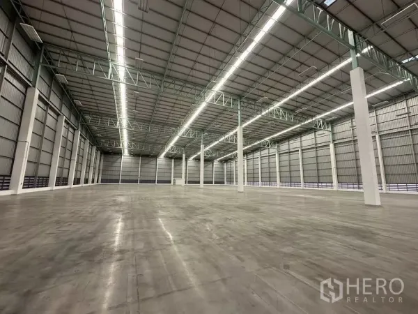 工厂 出租在Si Racha, Chon Buri - 高挑仓库内景，LED灯带、钢桁架与打磨混凝土地面，空间开阔。