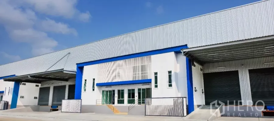 工厂 出租在Bang Sao Thong, Samut Prakan - 现代工厂外观，白蓝色立面，带有顶棚装卸区与多扇卷闸门