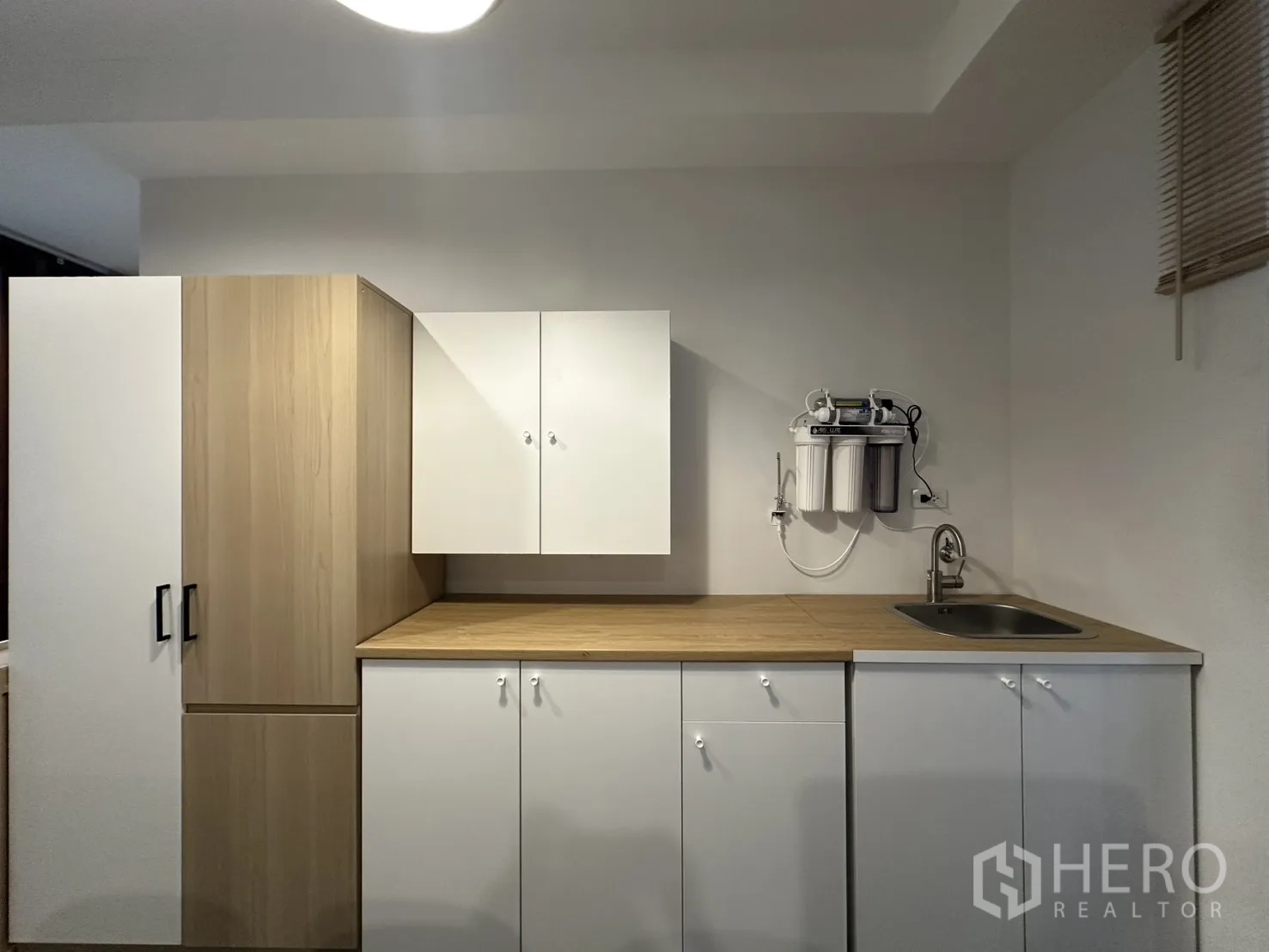 Apartment for rent in Pathum Wan, Bangkok - Compact pantry kitchen with white cabinets, wood countertop, and a water filter system.