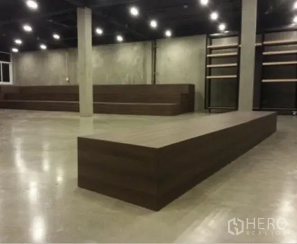 店屋 出租在Suan Luang, Bangkok - 大开间展示厅，水泥自流平地面，黑色天花射灯，木质展示平台与置物架。