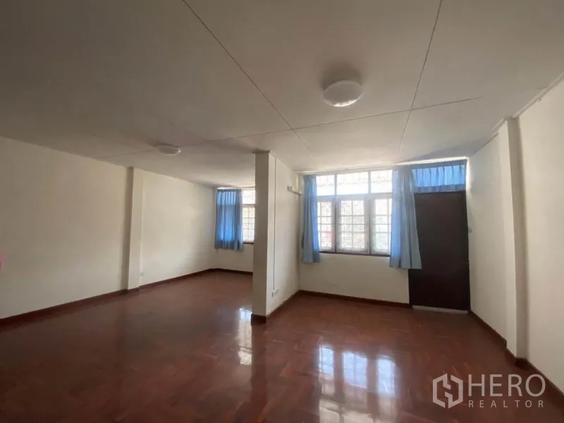 联排别墅 出租在Watthana, Bangkok - 明亮的楼上起居空间，木地板与蓝色窗帘窗户。