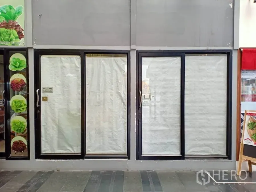 零售空间 出租在Ratchathewi, Bangkok - 位于曼谷Asoke室内走道的空置商铺门面，黑色框架滑动玻璃门与被纸遮盖的橱窗。