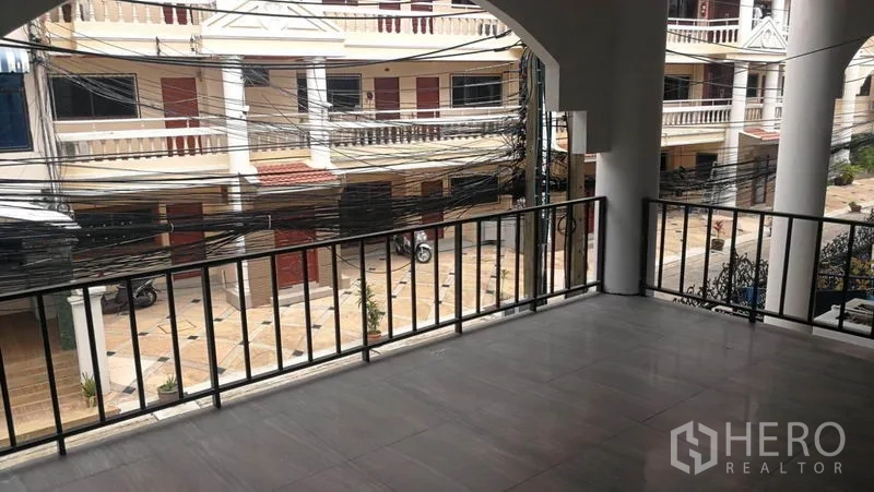 Townhouse for rent in Khlong Toei, Bangkok - Street-facing exterior of multi-level white townhouse with balcony and red gate.
