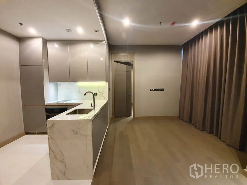 Condominium for rent in Huai Khwang, Bangkok - Open-plan living and kitchen with marble peninsula, tall built-in cabinets, integrated appliances, and heavy drapes.