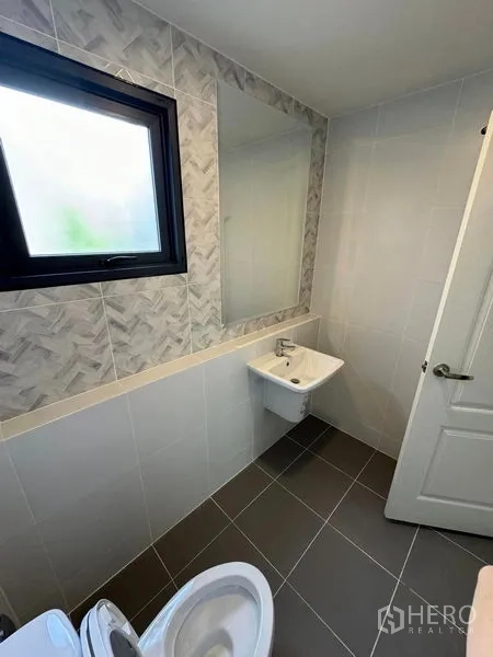 Detached House for rent in Don Mueang, Bangkok - Clean bathroom with patterned wall tiles, frosted window, mirror, basin and toilet.