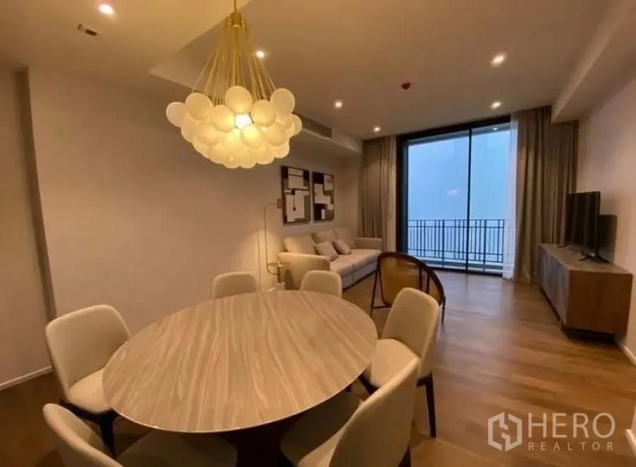 Condominium for rent in Pathum Wan, Bangkok - Open-plan living and dining room in a Bangkok condo with round table, modern chandelier, sofa, TV console, and balcony doors.