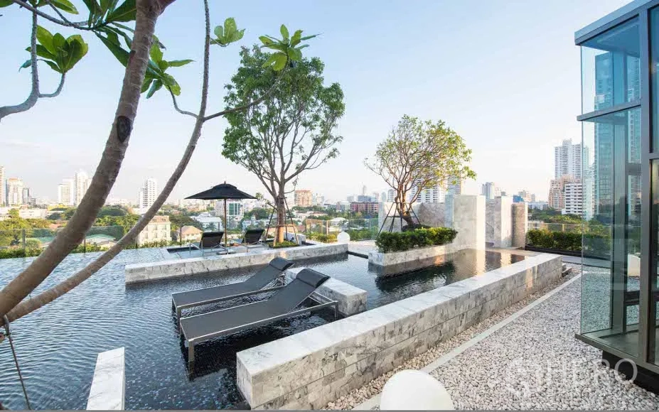 Condominium for rent or sale in Watthana, Bangkok - Sky pool deck with sun loungers, trees and panoramic skyline views at the condo.