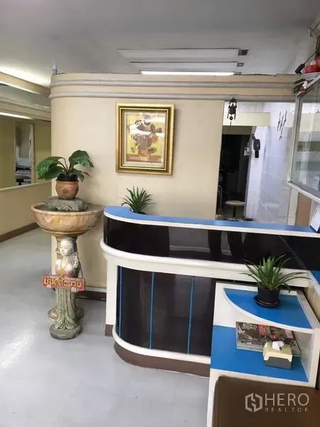 อาคารพาณิชย์ ให้เช่าในPhra Khanong, Bangkok - เคาน์เตอร์ต้อนรับโค้ง พร้อมกระถางต้นไม้และอ่างน้ำตกตกแต่งบนผนังสีครีม