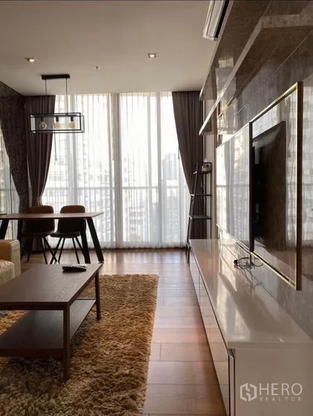 Condominium for rent in Khlong Toei, Bangkok - Bright lounge with TV console, sheer-draped full-height windows, and dining area on hardwood floors.