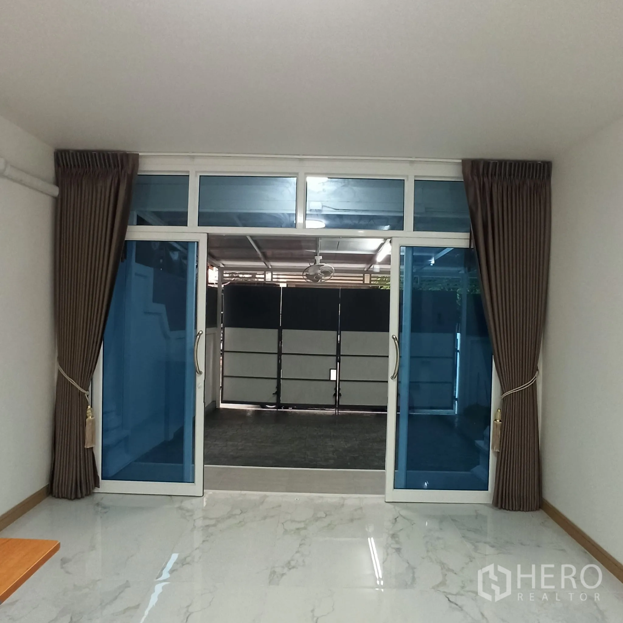 Townhouse for rent in Wang Thonglang, Bangkok - Bright living room with marble-look tiles and sliding glass doors to the carport.
