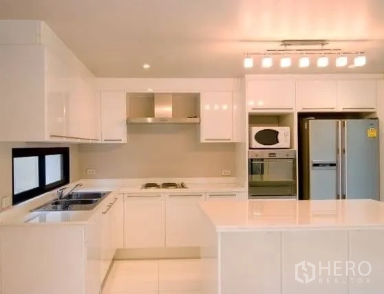 Detached House for rent in Khlong Toei, Bangkok - Sleek white kitchen with island, built‑in appliances and modern lighting.