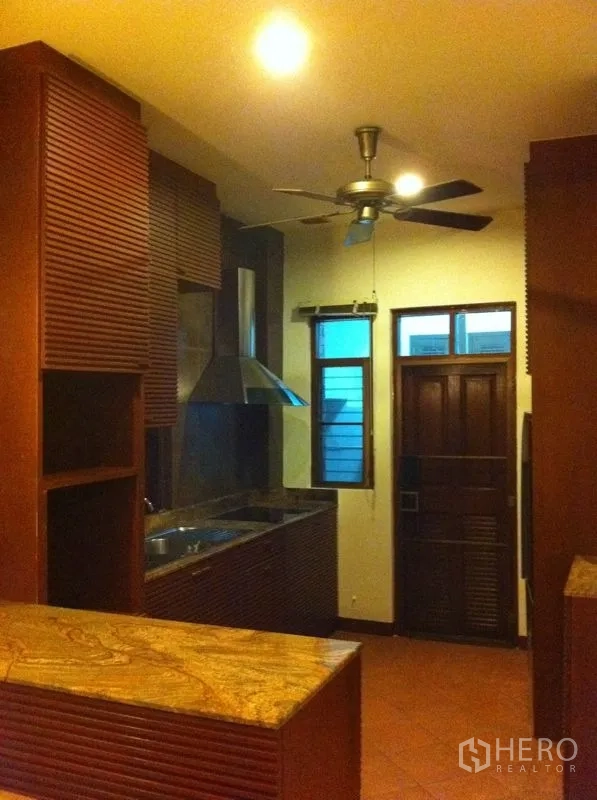 Townhouse for rent or sale in Watthana, Bangkok - Fitted kitchen with wooden cabinetry, stone countertop and stainless range hood with ceiling fan.