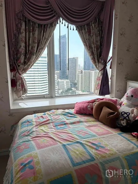Condominium for sale in Huai Khwang, Bangkok - Second bedroom with pastel bedding, floral curtains and city views.