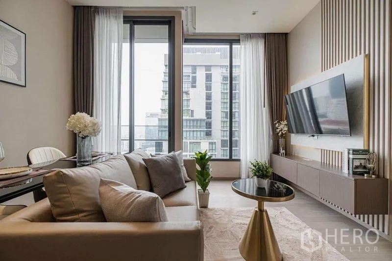 Condominium for rent in Watthana, Bangkok - Airy living area with sofa, coffee table and large balcony windows facing city buildings.