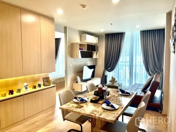 Condominium for rent in Watthana, Bangkok - Bright living–dining area with marble table, built‑in cabinetry, TV console and floor‑to‑ceiling curtains.