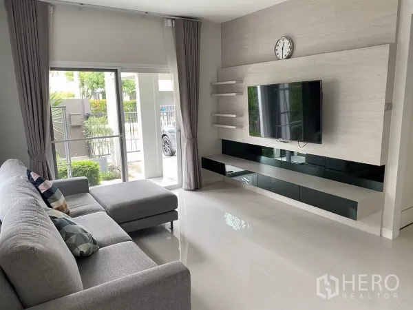 บ้าน ให้เช่าในPrawet, Bangkok - ห้องนั่งเล่นสว่าง โซฟาเข้ามุมสีเทา ทีวีติดผนัง และประตูกระจกบานเลื่อน