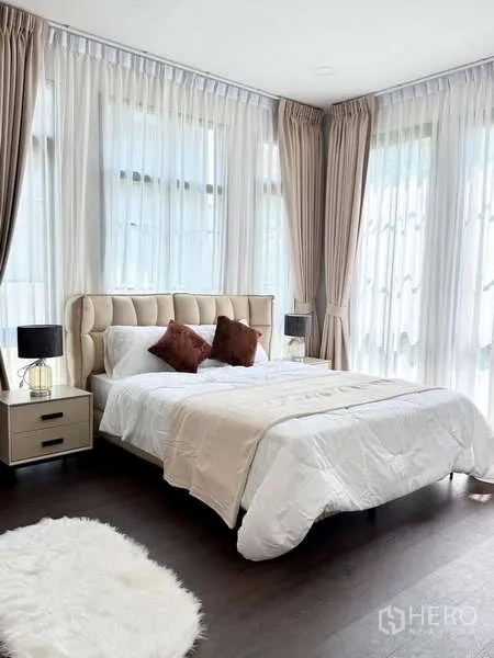 独立式住宅 出租或出售在Bang Phli, Samut Prakan - 轉角臥室，軟包床頭、白色床品與雙色窗簾。